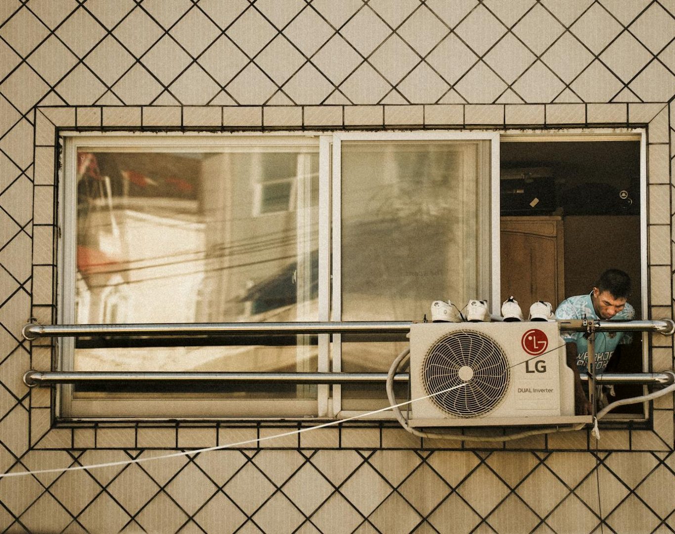 Man looks outside a window with an LG air conditioner unit visible, creating a reflective effect.